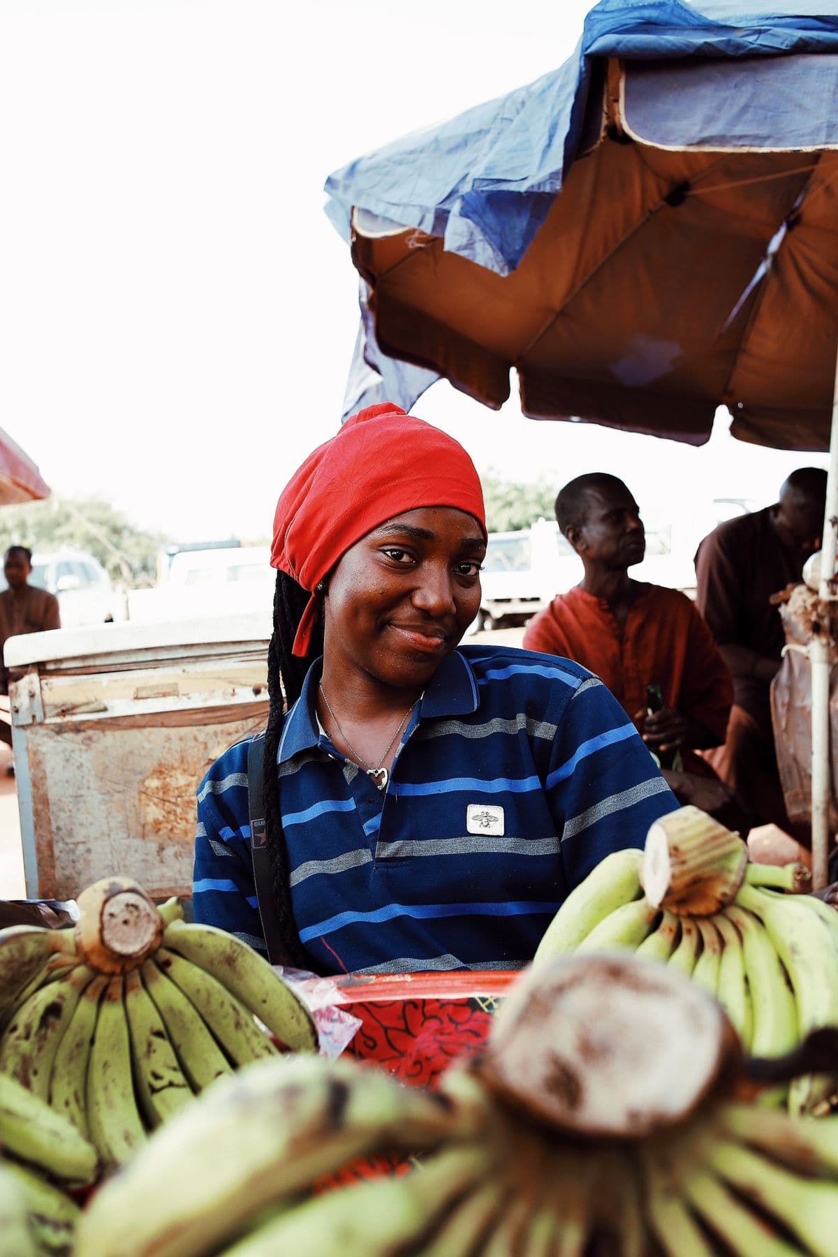 A market trader smiling behind a stall of plantains